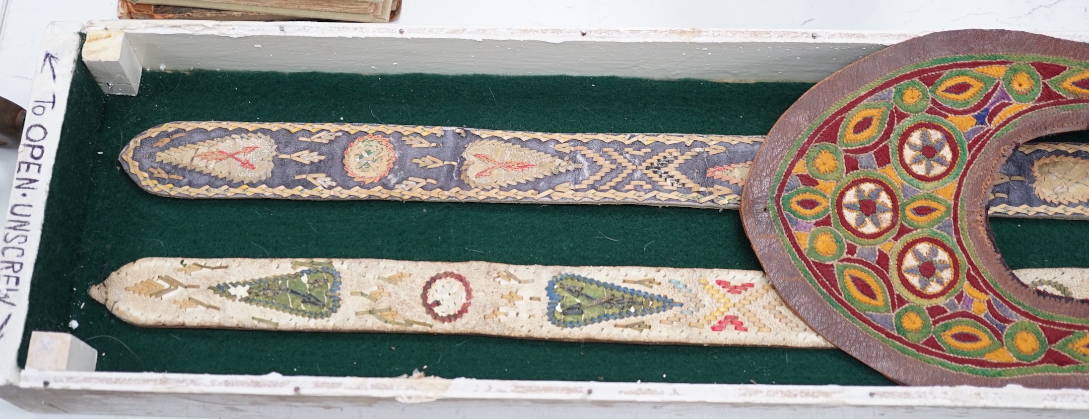 A two framed native American Indian ornately woven and embroidered leather belts and a pair of leather embroidered slipper fronts, longest belt 103cms